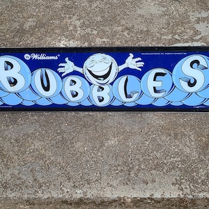 May include: A blue and black arcade game panel with the word "BUBBLES" in large, light blue bubble letters. A smiling face with arms and hands is above the letters. The word "Williams" is at the top.