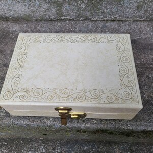 May include: A white jewelry box with a gold floral design and a brass latch.