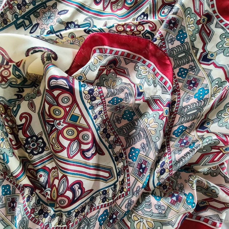May include: A white silk scarf with a red, blue, and green paisley pattern. The scarf is folded in half and the pattern is visible on both sides.