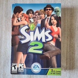 May include: The Sims 2 PC game box. The cover features a group of stylized characters in various outfits. The game title is prominently displayed with a green diamond symbol. The EA Games logo is visible.