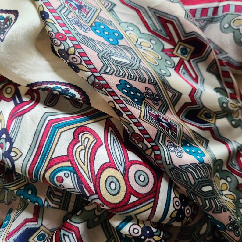 May include: A white fabric with a colorful geometric pattern. The pattern features red, blue, green, yellow, and black colors. The fabric is folded and draped, showing the intricate details of the design.