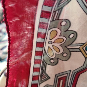 May include: Close-up of a red, white, and blue patterned fabric with a geometric design. The fabric has a floral motif in the center.