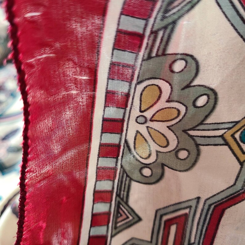 May include: Close-up of a red, white, and blue patterned fabric with a geometric design. The fabric has a floral motif in the center.