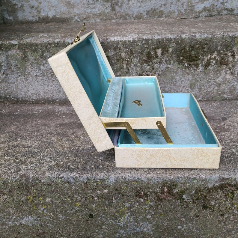 May include: A white two-tiered jewelry box with a blue velvet lining. The box is open and the top tier is hinged.