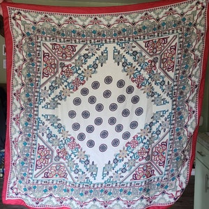 May include: A red, white, and blue patterned square scarf with a white center and a repeating pattern of circles. The scarf has a border of intricate geometric designs.