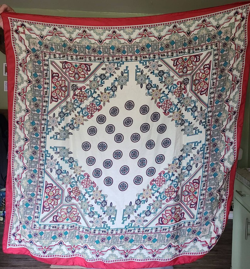 May include: A red, white, and blue patterned square scarf with a white center and a repeating pattern of circles. The scarf has a border of intricate geometric designs.