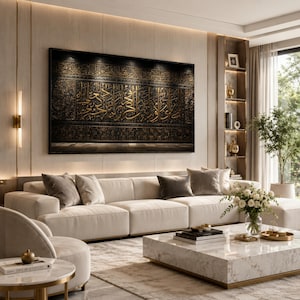 May include: A large rectangular wall art piece featuring intricate gold Arabic calligraphy set against a dark black background, displayed above a long cream-colored sectional sofa in a room with a marble coffee table and neutral decor.