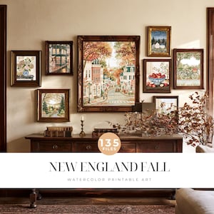 May include: A gallery wall display featuring eight framed watercolor prints with autumn themes, including a central street scene, a bowl of red apples, a bicycle, and floral arrangements, all set above a dark wooden console table with text.