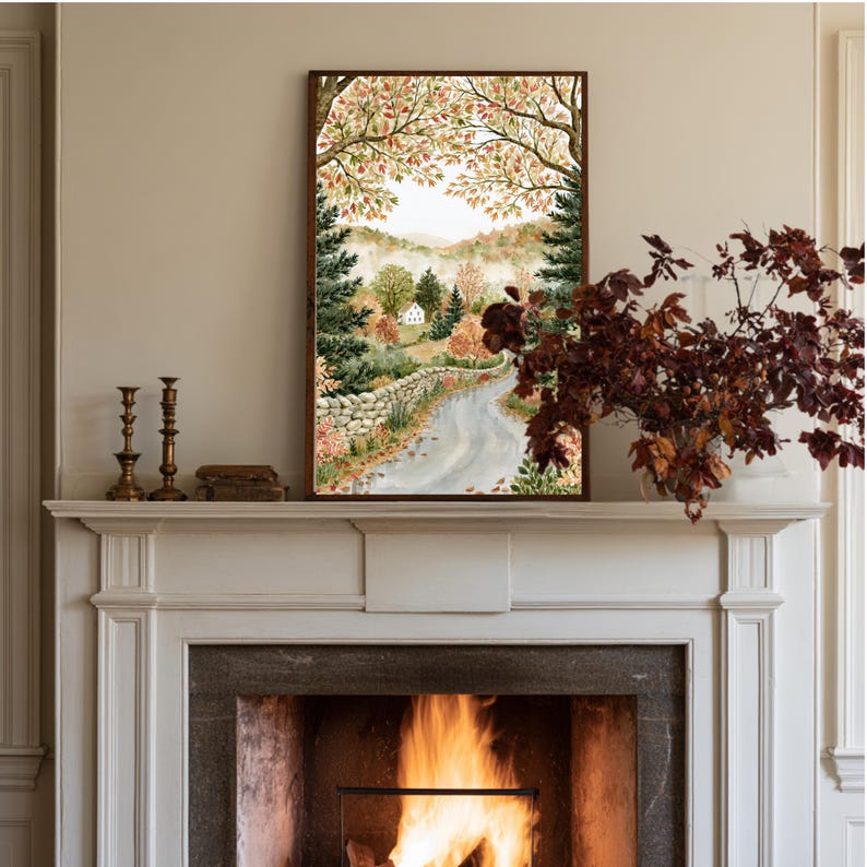 May include: A framed landscape painting depicting a winding path alongside a stone wall, leading toward a small white house nestled among autumn trees with orange, red, and green foliage under a soft sky, displayed above a fireplace mantel.