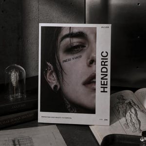 Könnte beinhalten: Ein rechteckiges Zine mit dem Titel HENDRIC, das ein schwarz-weißes Porträt einer Person mit dem Text ratio vincit auf der Wange zeigt. Das Cover enthält das Datum JULY 2026 und den Satz PERFECTION IS NOT BEAUTY, IT'S SURVIVAL in Weiß.