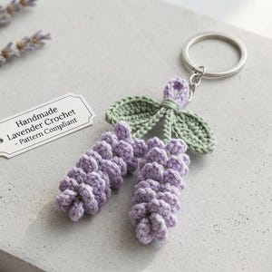 May include: A crochet keychain featuring two lavender-colored flower stalks with light green leaves attached to a silver metal ring. A small white rectangular tag is included with the text: Handmade Lavender Crochet - Pattern Compliant.