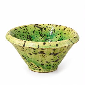 May include: A ceramic bowl with a wide, flared rim and a tapered base. The exterior and interior surfaces feature a vibrant lime green glaze with a glossy finish, decorated with irregular black paint splatters throughout the entire piece.