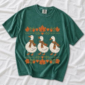 Three white ducks in striped scarves with acorn and maple leaf borders, retro screen print fall t-shirt art