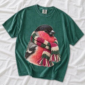 Colored-pencil bullfinch bird wrapped in a chunky striped knit scarf, cozy winter birdwatcher t-shirt art