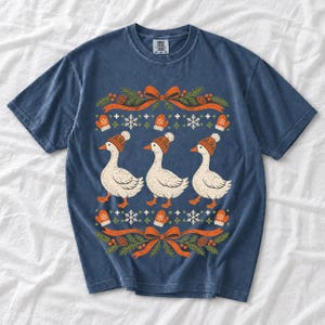 Three geese in pompom knit beanies with mittens, snowflakes and pine borders, retro winter t-shirt graphic