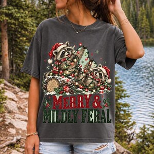 Two raccoons tangled in Christmas lights beside a log with the text Merry & Mildly Feral