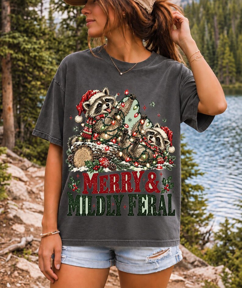 Two raccoons tangled in Christmas lights beside a log with the text Merry & Mildly Feral