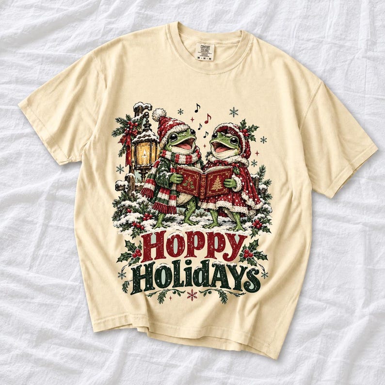 Two frogs singing carols in the snow with a lantern and songbook, text Hoppy Holidays