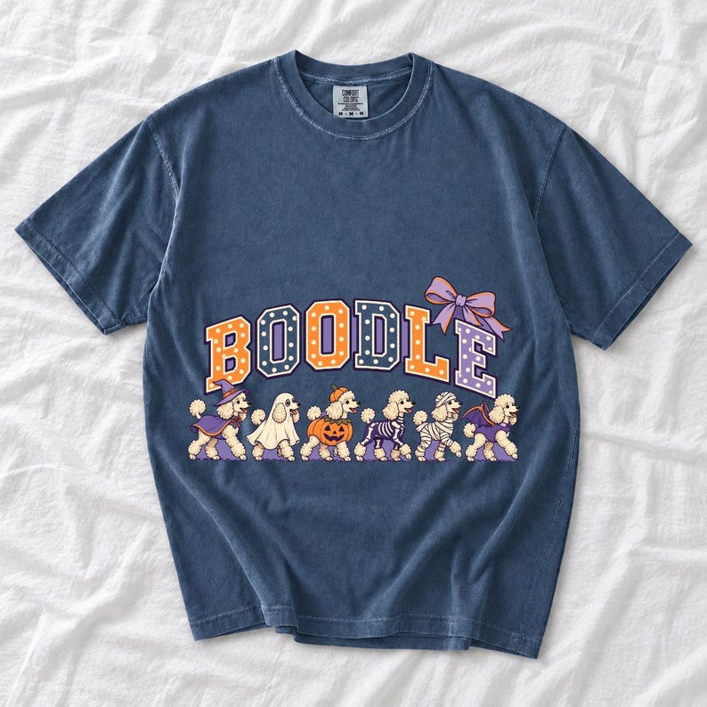 Six poodles in Halloween costumes walking under the arched word BOODLE, lavender and orange polka-dot varsity style