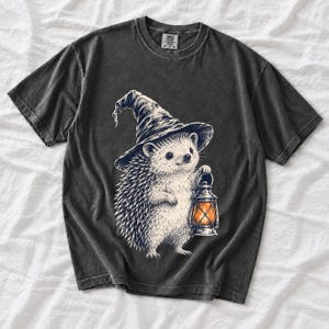 Etched pen illustration of a hedgehog in a witch hat holding a lantern, bone white with orange accent