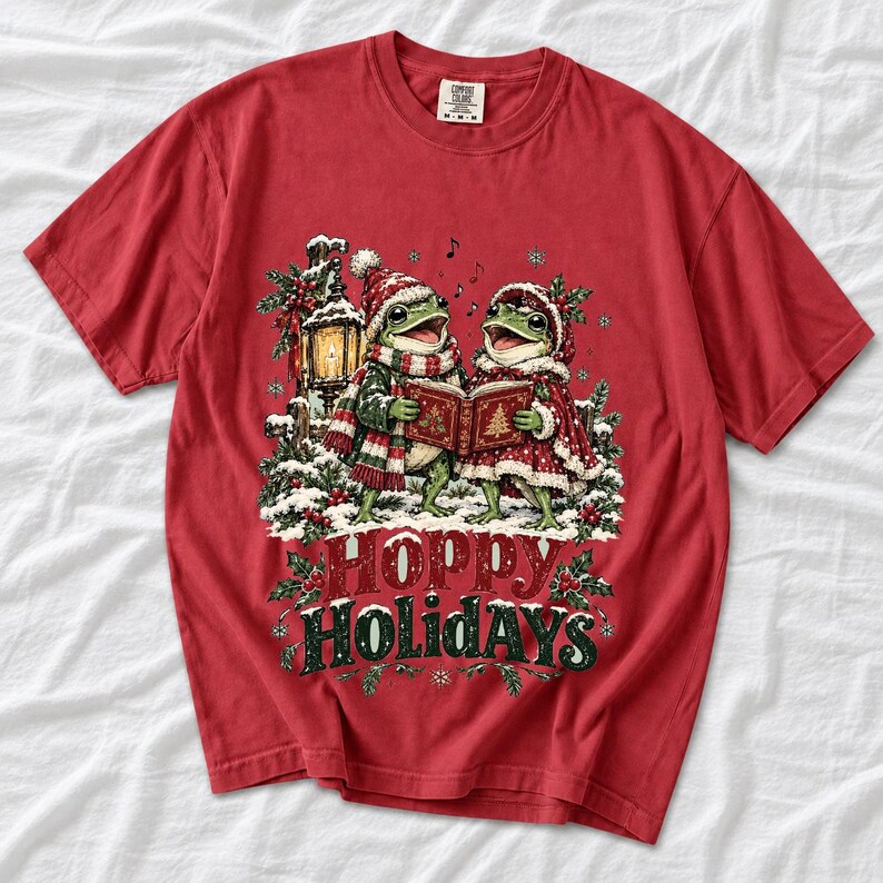 Two frogs singing carols in the snow with a lantern and songbook, text Hoppy Holidays