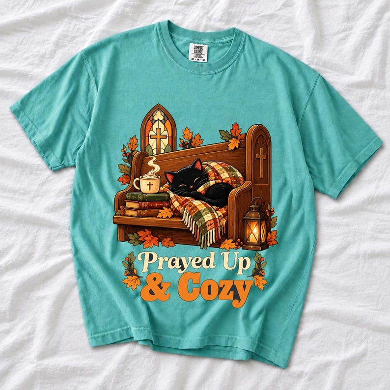 Black cat curled on a church pew with blanket and cocoa among autumn leaves, text "Prayed Up & Cozy", retro illustration