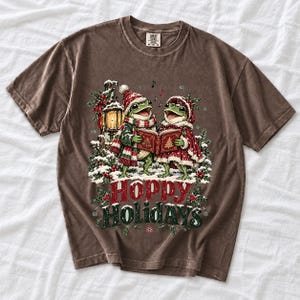 Two frogs singing carols in the snow with a lantern and songbook, text Hoppy Holidays
