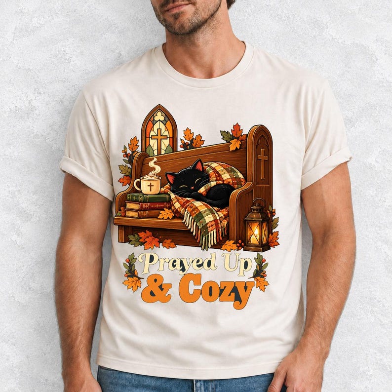 Black cat curled on a church pew with blanket and cocoa among autumn leaves, text "Prayed Up & Cozy", retro illustration