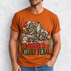 Two raccoons tangled in Christmas lights beside a log with the text Merry & Mildly Feral