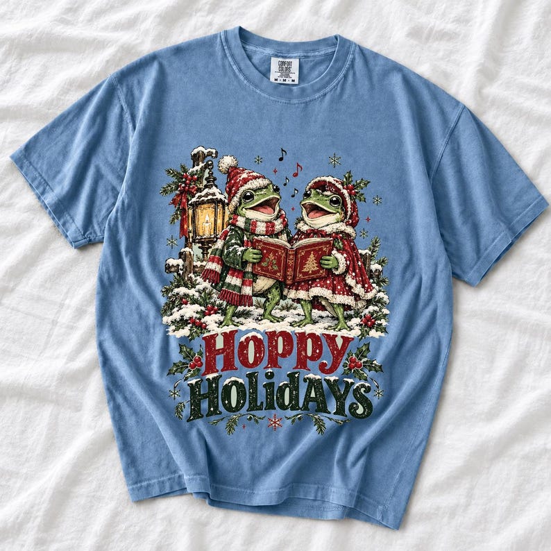 Two frogs singing carols in the snow with a lantern and songbook, text Hoppy Holidays