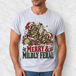 Two raccoons tangled in Christmas lights beside a log with the text Merry & Mildly Feral