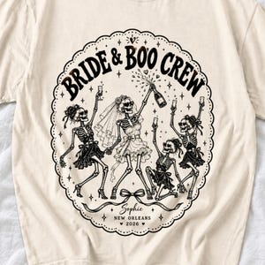 Skeleton bride popping champagne with cheering skeleton bridesmaids and the text Bride & Boo Crew