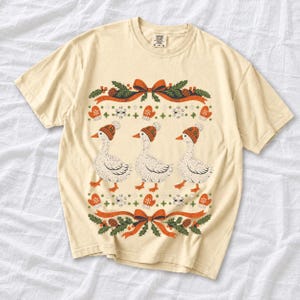 Three geese in pompom knit beanies with mittens, snowflakes and pine borders, retro winter t-shirt graphic