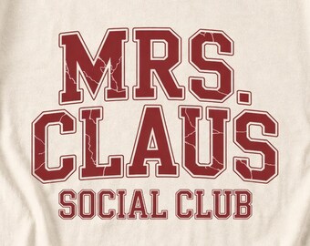 May include: A cream-colored fabric garment featuring the dark red text MRS. CLAUS'S SOCIAL CLUB in a bold, collegiate-style font. The lettering has a distressed, cracked texture effect throughout the surface of the printed design.