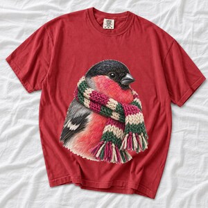 Colored-pencil bullfinch bird wrapped in a chunky striped knit scarf, cozy winter birdwatcher t-shirt art