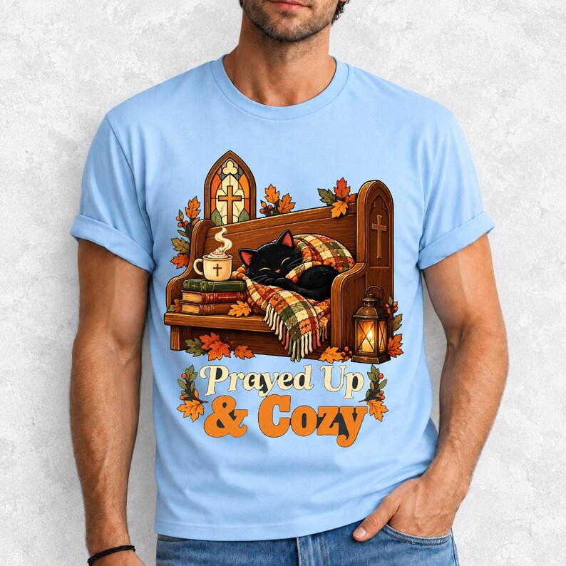 Black cat curled on a church pew with blanket and cocoa among autumn leaves, text "Prayed Up & Cozy", retro illustration
