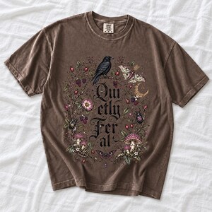 Raven on a wild rose branch with beetles and berries around blackletter text "Quietly Feral"