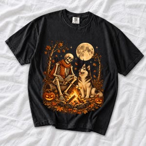 A skeleton in a scarf roasting marshmallows by a campfire beside a husky in an autumn forest under a full moon