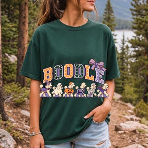 Six poodles in Halloween costumes walking under the arched word BOODLE, lavender and orange polka-dot varsity style