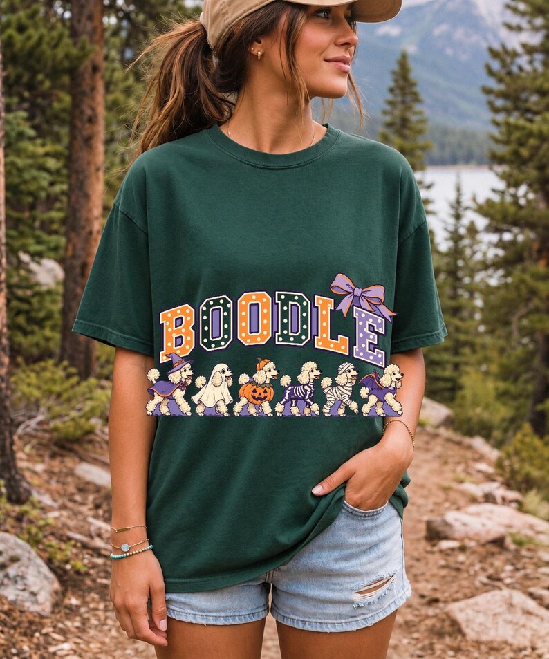 Six poodles in Halloween costumes walking under the arched word BOODLE, lavender and orange polka-dot varsity style
