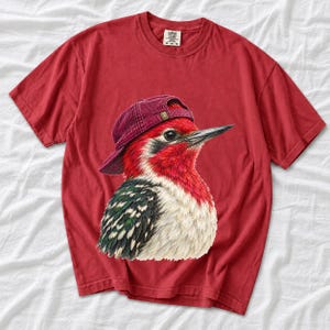 Colored-pencil red-headed woodpecker in side profile wearing a backwards corduroy cap, funny birder t-shirt graphic