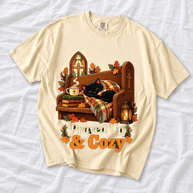 Black cat curled on a church pew with blanket and cocoa among autumn leaves, text "Prayed Up & Cozy", retro illustration
