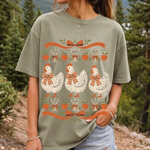Three fluffy hens with gingham bows between apple and wheat borders, retro folk art fall t-shirt design