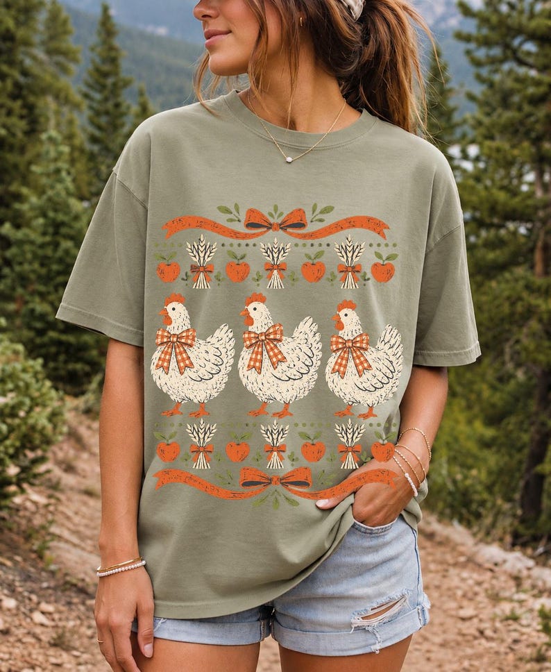 Three fluffy hens with gingham bows between apple and wheat borders, retro folk art fall t-shirt design