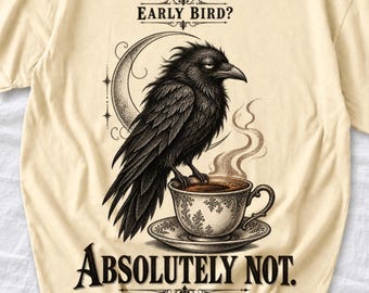 May include: A cream-coloured t-shirt featuring a black graphic of a crow perched on a teacup with steam rising. Above the crow is the text "EARLY BIRD?" and below the teacup is the text "ABSOLUTELY NOT." The design includes a crescent moon.