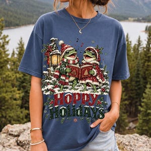 Two frogs singing carols in the snow with a lantern and songbook, text Hoppy Holidays