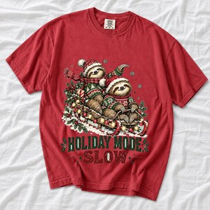 Two sloths in ugly sweaters riding a sled with lights and the text Holiday Mode: Slow