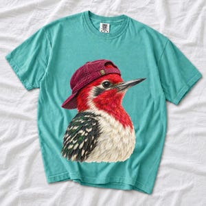 Colored-pencil red-headed woodpecker in side profile wearing a backwards corduroy cap, funny birder t-shirt graphic