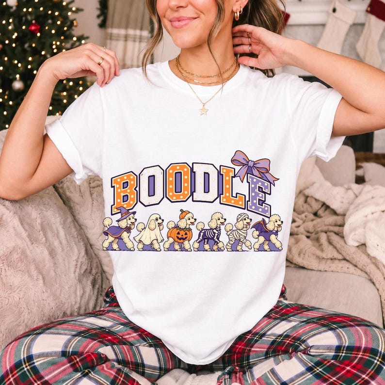 Six poodles in Halloween costumes walking under the arched word BOODLE, lavender and orange polka-dot varsity style