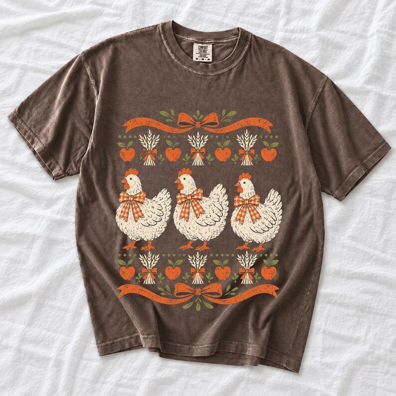 Three fluffy hens with gingham bows between apple and wheat borders, retro folk art fall t-shirt design